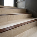 Wide 52mm aluminium tile-in stair nosing with NB Nut Brown RAL 8007 ribbed insert on cream travertine-look tiled stairs