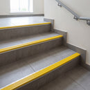 Wide 52mm aluminium tile-in stair nosing with CG Yellow RAL 1021 ribbed insert on a grey tiled public building stairwell