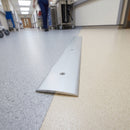 70mm satin aluminium cover plate screw fitted between two vinyl floors in a healthcare corridor