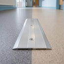 80mm matt silver aluminium cover plate screw fitted between grey and beige vinyl in a school corridor