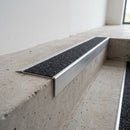 Slimline raked back 59x30mm aluminium stair nosing with a black Olympic Grip aluminium oxide insert, on a satin aluminium bar, fitted directly to a bare concrete step