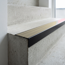 Slimline raked back 59x30mm aluminium stair nosing with an ivory cream ribbed PVC insert, on a black anodised bar, fitted directly to a bare concrete step