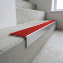 Slimline raked back 59x30mm aluminium stair nosing with a poppy red ribbed PVC insert, on a satin aluminium bar, fitted directly to a bare concrete step