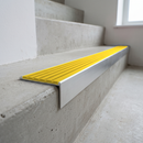 Slimline raked back 59x30mm aluminium stair nosing with a bright yellow ribbed PVC insert, on a satin aluminium bar, fitted directly to a bare concrete step