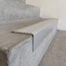 Concealed-fix aluminium stair nosing 65x55mm square front with a light grey castellated PVC cover strip, fitted to a concrete step
