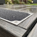 Close-up of coarse black grit, bare aluminium margin and screw on a flat anti-slip plate on wet decking