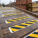 Black and yellow hazard stripe flat anti-slip plates screwed across a wet timber loading ramp in a builders merchant yard