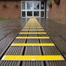 Narrow yellow 63mm anti-slip plates fixed across a timber decking path to a community hall entrance