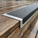 Close-up of coarse black grit, countersunk screw and bent aluminium leg wrapping a wet timber step edge