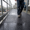 Black anti-slip GRP sheets screwed down along a wet external steel access walkway with a worker walking across them