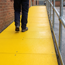 Yellow anti-slip GRP sheets fixed along an external access ramp with handrail and an engineer walking up