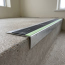 Ramped aluminium stair nosing 66x32mm with photoluminescent strip and a black anti-slip PVC insert, fitted to a concrete step