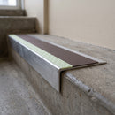 Ramped aluminium stair nosing 66x32mm with photoluminescent strip and a brown anti-slip PVC insert, fitted to a concrete step