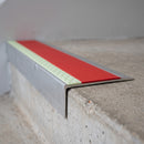 Ramped aluminium stair nosing 66x32mm with photoluminescent strip and a red anti-slip PVC insert, fitted to a concrete step