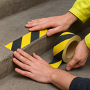 Person applying black and yellow chevron anti-slip tape to step edge in UK workplace