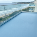 Light Blue TerraceShield anti-slip balcony paint applied to a balcony floor, a seaside penthouse balcony with glass railing and ocean view