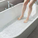 Clear transparent PVC pebble-textured non-slip bath mat with suction cups laid in a bathtub, with bare feet stepping onto it safely in a modern bathroom