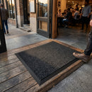 Black polypropylene entrance mat 0.6m x 0.9m placed at restaurant doorway with person stepping on it