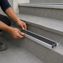 Installer fitting a black-insert tile-in stair nosing into the edge of a grey tiled step