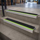 Two aluminium stair nosings with black and green anti-slip inserts fitted to concrete warehouse steps