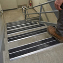 Work boot on concrete stairs with black twin-insert nosings, in a plain stairwell with grey steel handrails