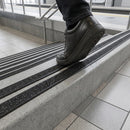 Boot on a concrete step fitted with two parallel black anti-slip strips, glass balustrade behind
