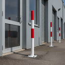 Red and white steel traffic bollard bolted to the ground outside a warehouse entrance protecting the doorway from vehicle impact