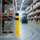 Yellow and black safety bollard guarding a warehouse racking corner near a forklift aisle