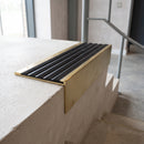 Solid brass 59mm slimline stair nosing with Black Castellated anti-slip insert fitted to a concrete step in a commercial stairwell
