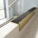 Solid brass 59mm slimline stair nosing with Black Olympic Grip anti-slip insert fitted to a concrete step in a commercial stairwell