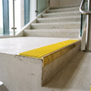 Solid brass 59mm slimline stair nosing with Yellow Castellated anti-slip insert fitted to a concrete step in a commercial stairwell