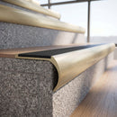 Solid brass bullnose stair nosing in Satin Brass finish with black castellated anti-slip infill fitted to a stair tread in a commercial stairwell