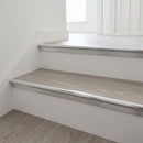 Bright silver anodised stair nosing fitted to pale grey oak LVT steps, the vinyl butting the smooth rounded bead with a shallow ribbed band down the top of the riser