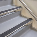 Bullnose aluminium stair nosing with a dark charcoal Mor Grip insert in bright polished finish fitted on a hotel or office stair finished in light grey vinyl