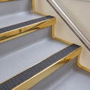 Bullnose aluminium stair nosing with a dark charcoal Mor Grip insert in mirrorflect gold finish fitted on a hotel or office stair finished in light grey vinyl