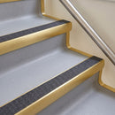 Bullnose aluminium stair nosing with a dark charcoal Mor Grip insert in satin gold finish fitted on a hotel or office stair finished in light grey vinyl