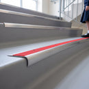 Bullnose stair nosing with high-visibility red anti-slip insert on pale safety vinyl stairs in a school
