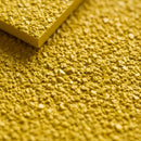 Macro close-up of coarse aluminium oxide grit on a yellow GRP panel with its thin 4mm edge visible