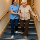 Carer helping elderly resident on care home carpeted staircase fitted with heavy duty aluminium carpet stair nosings - safety upgrade