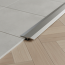 Close-up of 26mm aluminium T-bar threshold strip installed between grey tiles and herringbone laminate