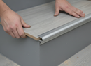 Installing push-in laminate stair nosing - hands pushing laminate tread board into silver aluminium channel during installation