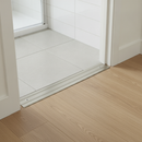 Flat aluminium door threshold strip installed at UK bathroom doorway between ceramic tile and oak laminate flooring