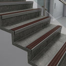 Raked back nosings with claret ribbed inserts on dark concrete steps beside a glass balustrade