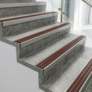Raked back nosings with claret castellated inserts on pale concrete steps beside a glass balustrade