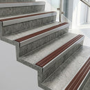 Raked back nosings with claret castellated inserts on pale concrete steps beside a glass balustrade