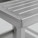 Close-up of the brushed stainless steel finish and drainage grooves on a commercial catering sink drainer board, showing the seam between the bowl and drainer