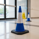Blue PVC traffic cone with reflective sleeve on a polished tiled floor inside a shopping centre entrance, cordoning off an area near the glass doors
