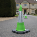 Green PVC traffic cone with reflective sleeve on a private driveway in front of a country house, marking off the drive during grounds maintenance