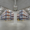 Convex safety mirror mounted high on a warehouse corner wall, reflecting pallet racking and a yellow forklift below