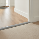 Self-adhesive PVC floor transition strip installed in UK hallway between laminate and carpet